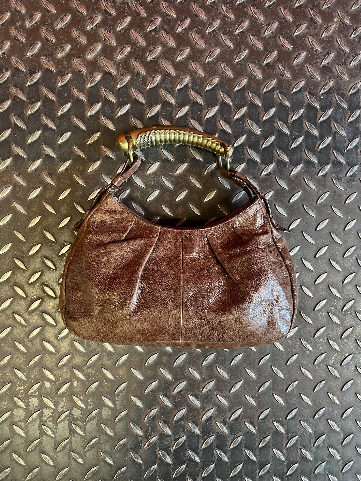 Dark brown shoulder bag displayed on a black chrome-framed chair beside flowers.
