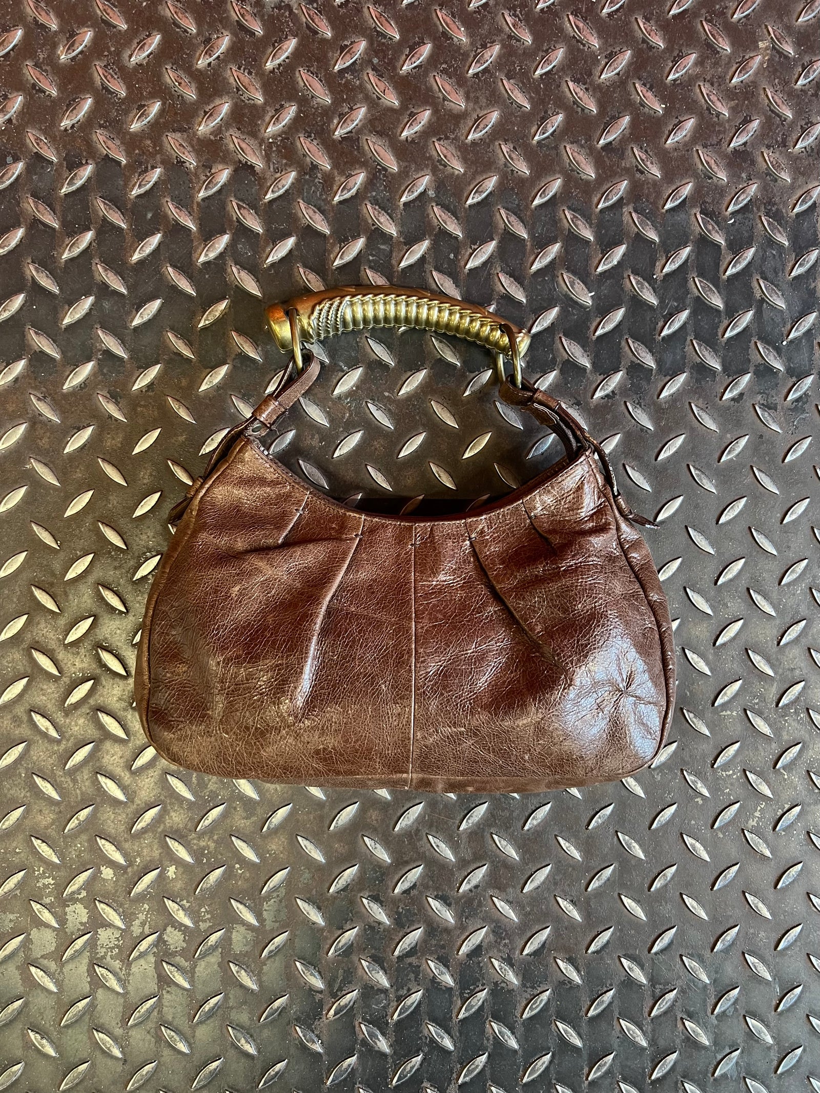 Dark brown shoulder bag displayed on a black chrome-framed chair beside flowers.