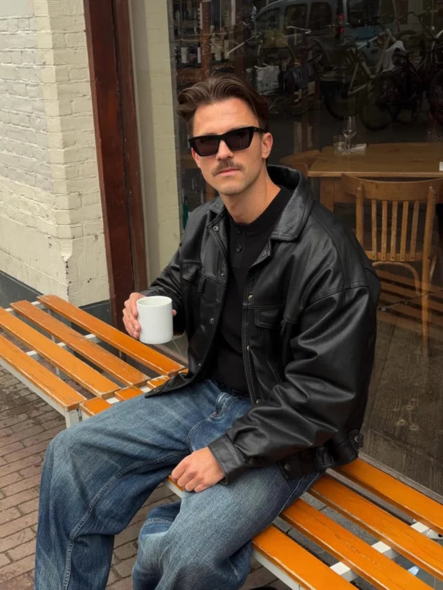 Person styling a black oversized jacket with denim outside a café.